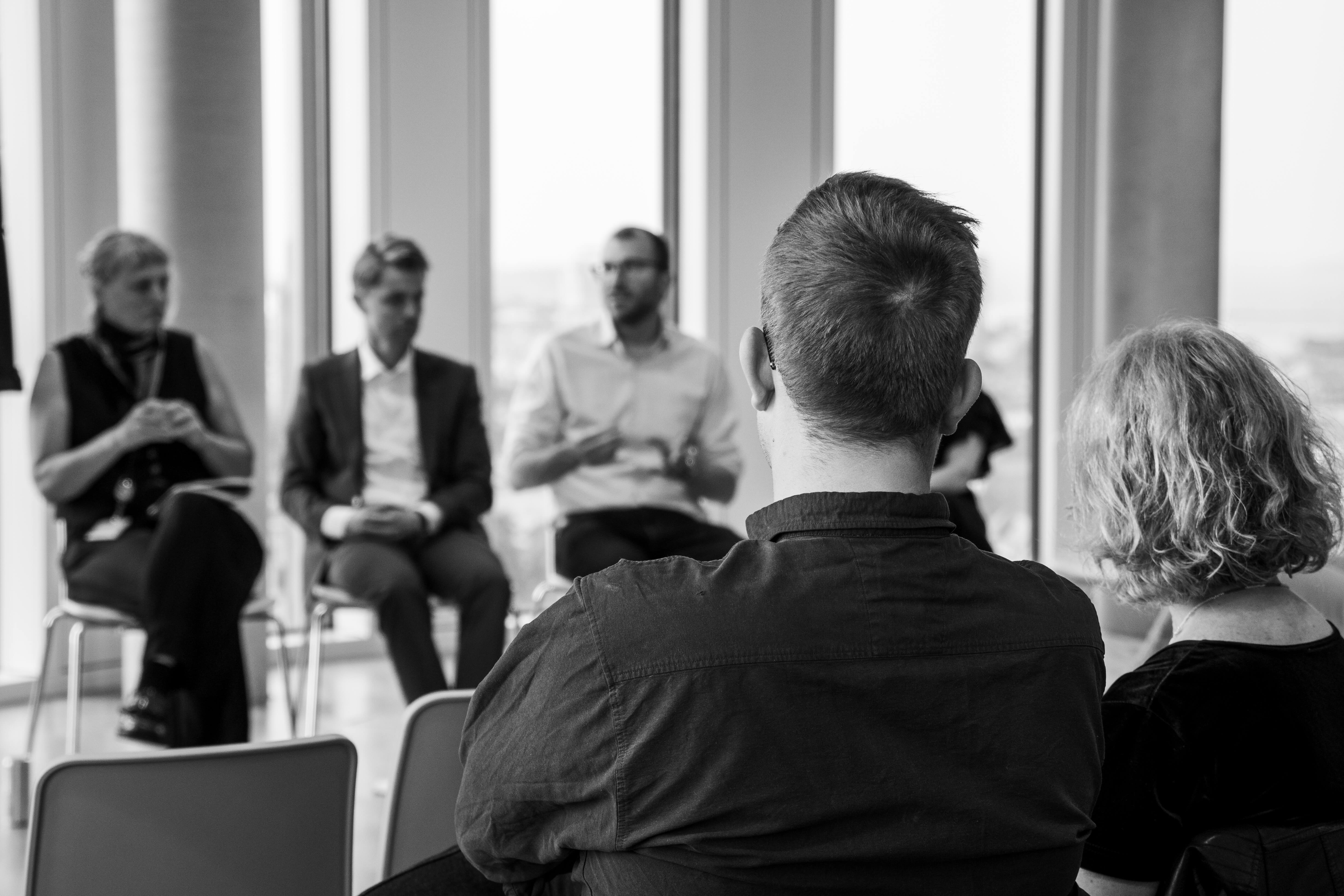 A room filled with people seated in a circle, engaged in discussion and debate