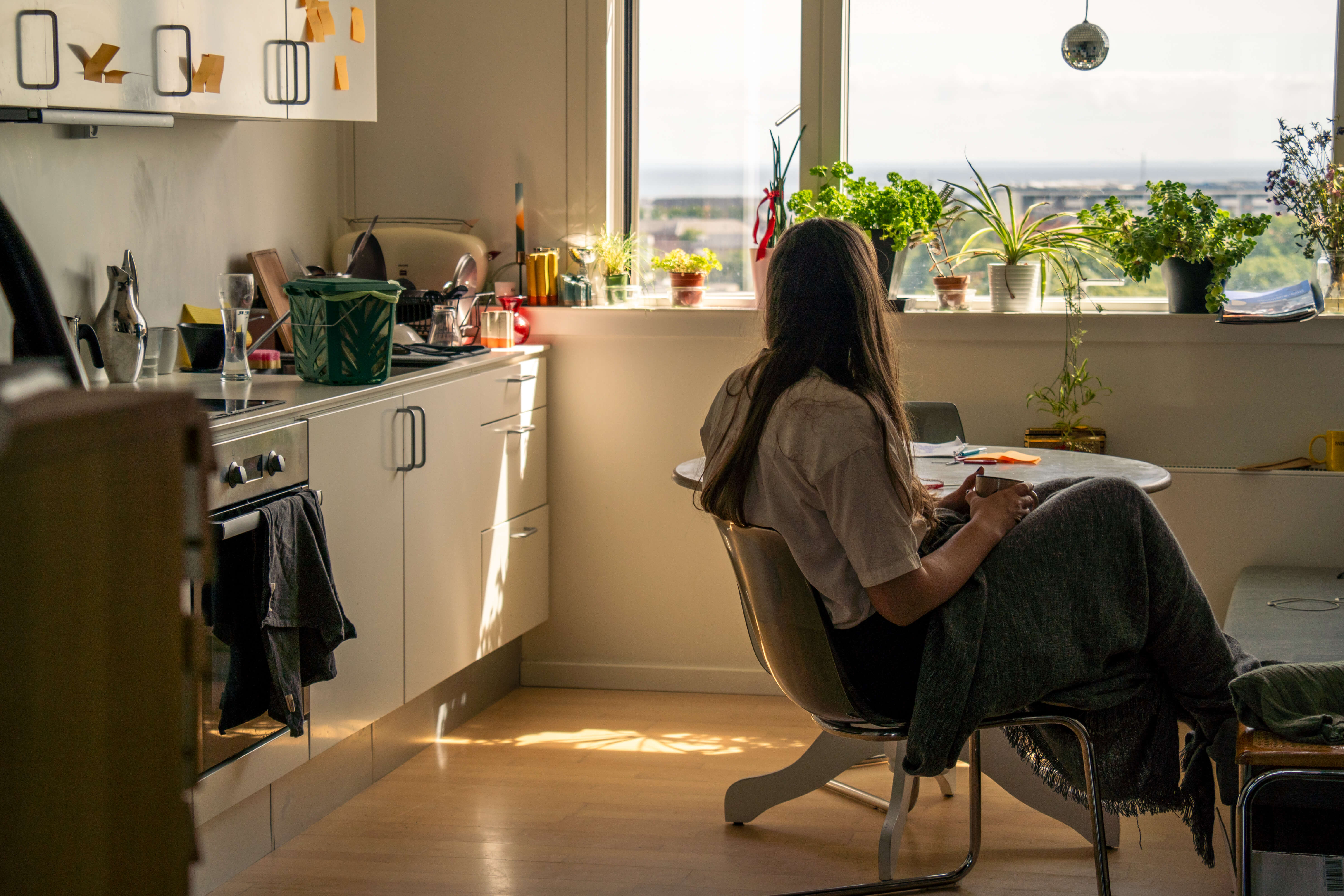 Kvinde sidder i køkken og kigger ud af et vindue